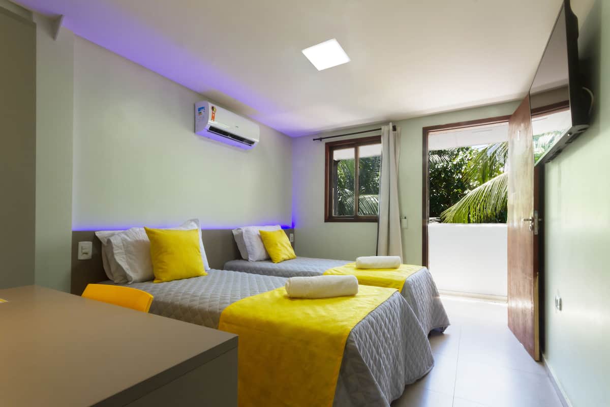 A hotel room with two beds, a table, and an air conditioning unit.