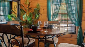 A wooden interior with a round dining table, chairs, a chandelier, and large windows with curtains. - Quiet One-Level Cabin, Hot Tub, Fire Pit, WiFi, Parkway Close (Sevierville)