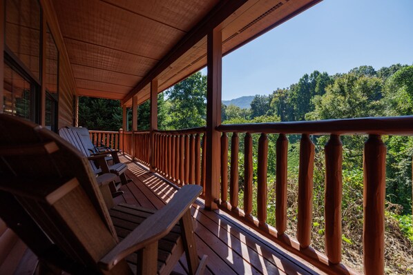 Una terraza de madera con sillas que da vista a un área boscosa.