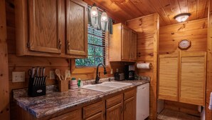 A wooden cabin kitchen with a granite countertop, wooden cabinets, a sink, a coffee maker, and a clock on the wall. - Quiet One-Level Cabin, Hot Tub, Fire Pit, WiFi, Parkway Close (Sevierville)