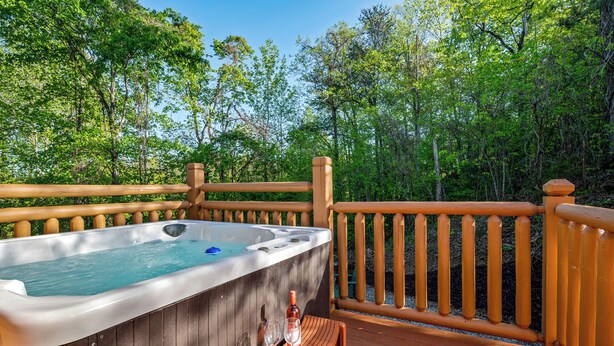 A wooden deck with a hot tub, a bottle, and two glasses. - Quiet One-Level Cabin, Hot Tub, Fire Pit, WiFi, Parkway Close (Sevierville)