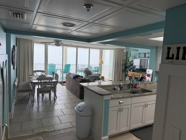 Un vaste espace de vie avec balcon, une cuisine dotée de meubles blancs et un coin repas avec chaises et table.