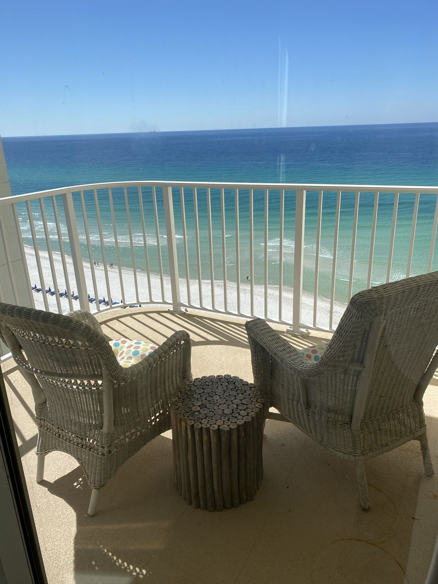 A balcony with wicker furniture, a small round table, and a view of the beach and ocean.