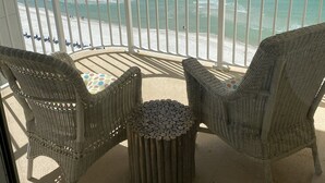 A balcony with wicker furniture, a small round table, and a view of the beach and ocean.
