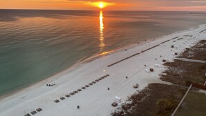 A beach with rows of beach chairs and umbrellas, a pier in the background, and a sunset over the ocean.