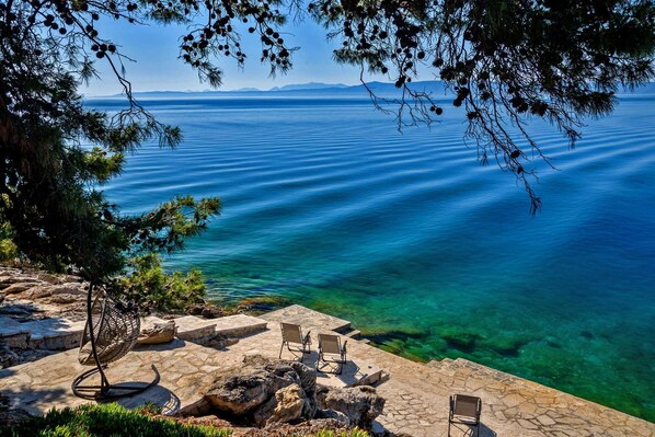 A stone patio with outdoor seating and a view of a calm sea.