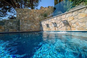 A swimming pool with clear blue water, surrounded by stone walls and a stone staircase.