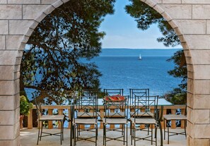 An outdoor seating area with stone arches, overlooking a body of water with a sailboat in the distance.
