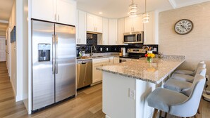 Una cocina moderna con armarios blancos, electrodomésticos de acero inoxidable, una encimera de granito y un reloj en la pared.