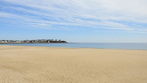 Una amplia playa de arena, cielo despejado y una costa distante con edificios.