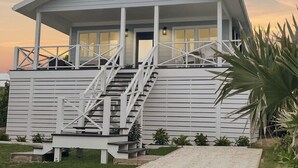 A white building with a covered porch, a staircase, and a door.