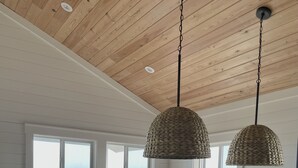 A kitchen with a large island, white cabinetry, and a view of the ocean. There are two hanging pendant lights and a window with a view of palm trees.