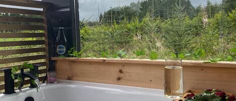 A wooden bathtub with a wooden bench, a glass of water, and a tray with flowers.