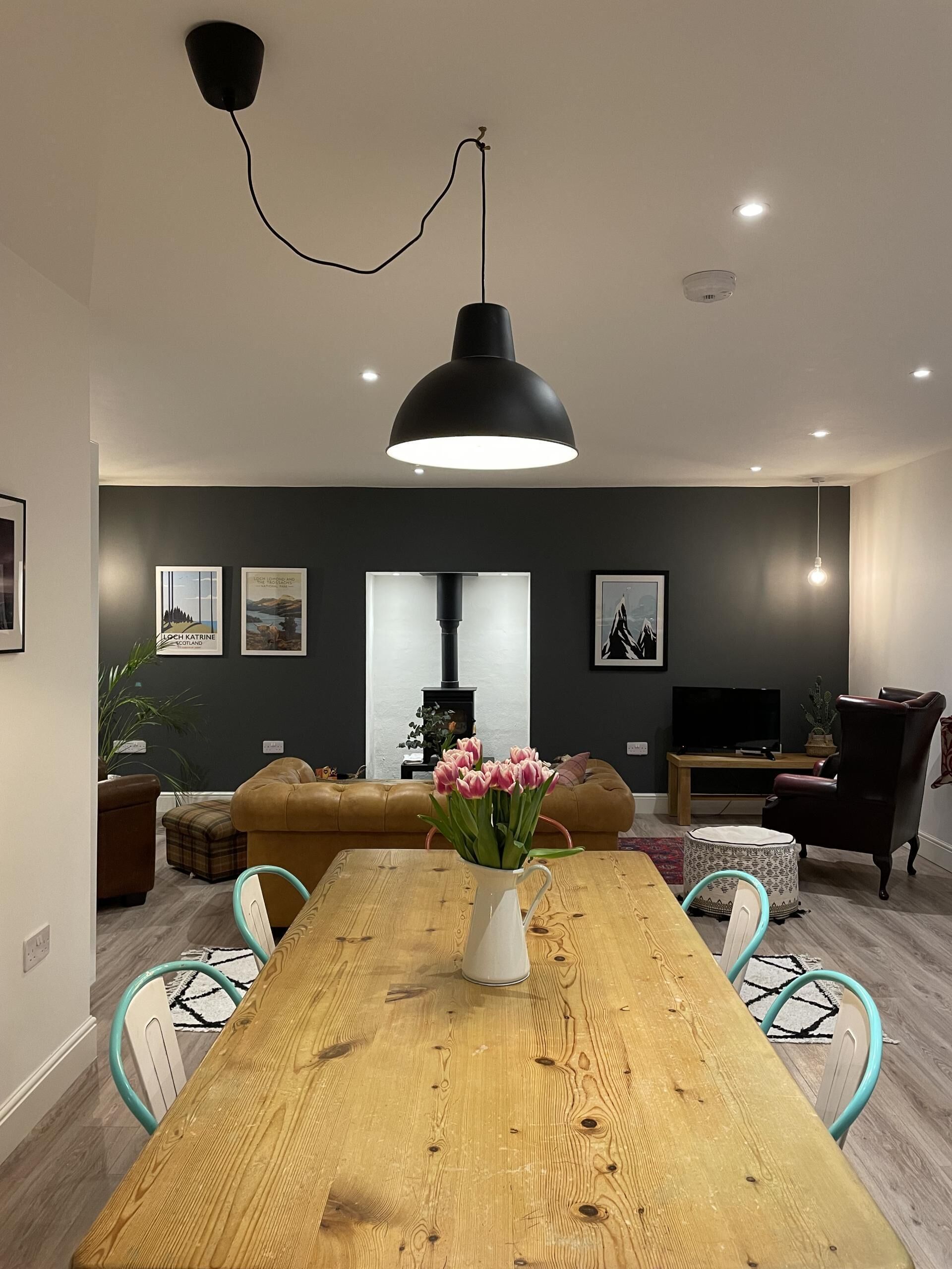 Een moderne woonkamer met een houten eettafel, een zwarte hanglamp, een bank en een televisie.