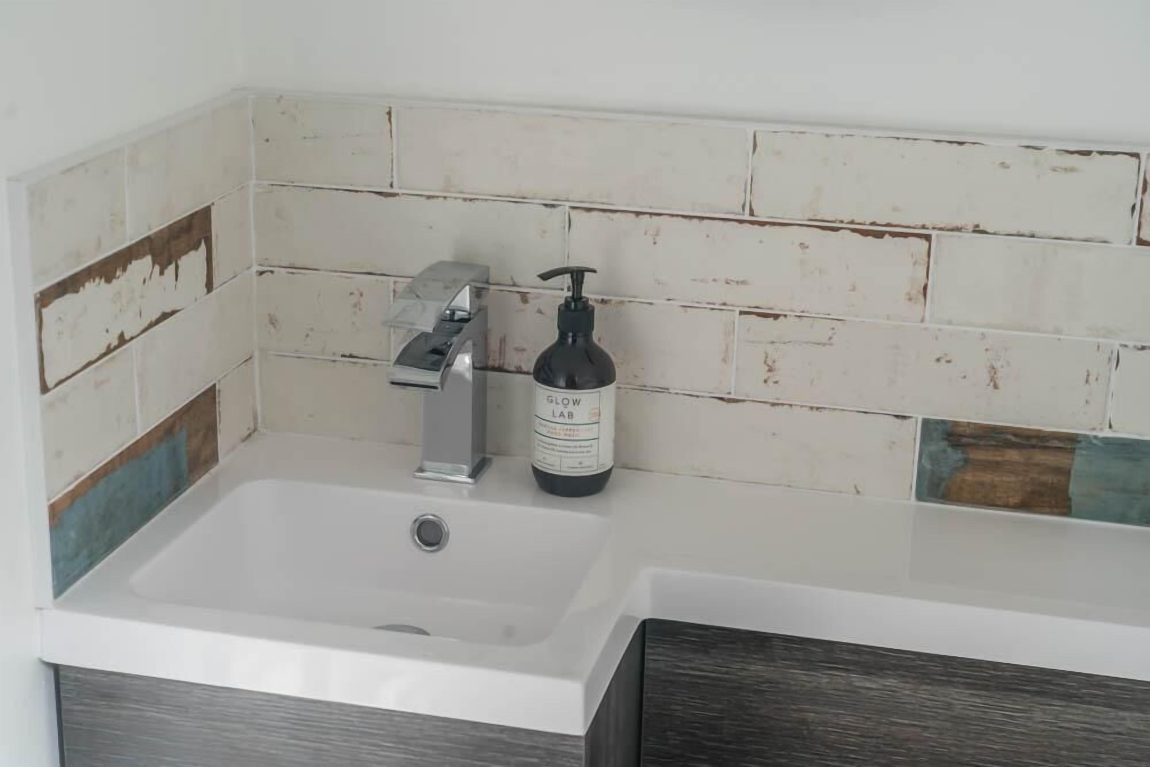A bathroom with a white sink, a silver faucet, and a bottle of Glow Lab soap.