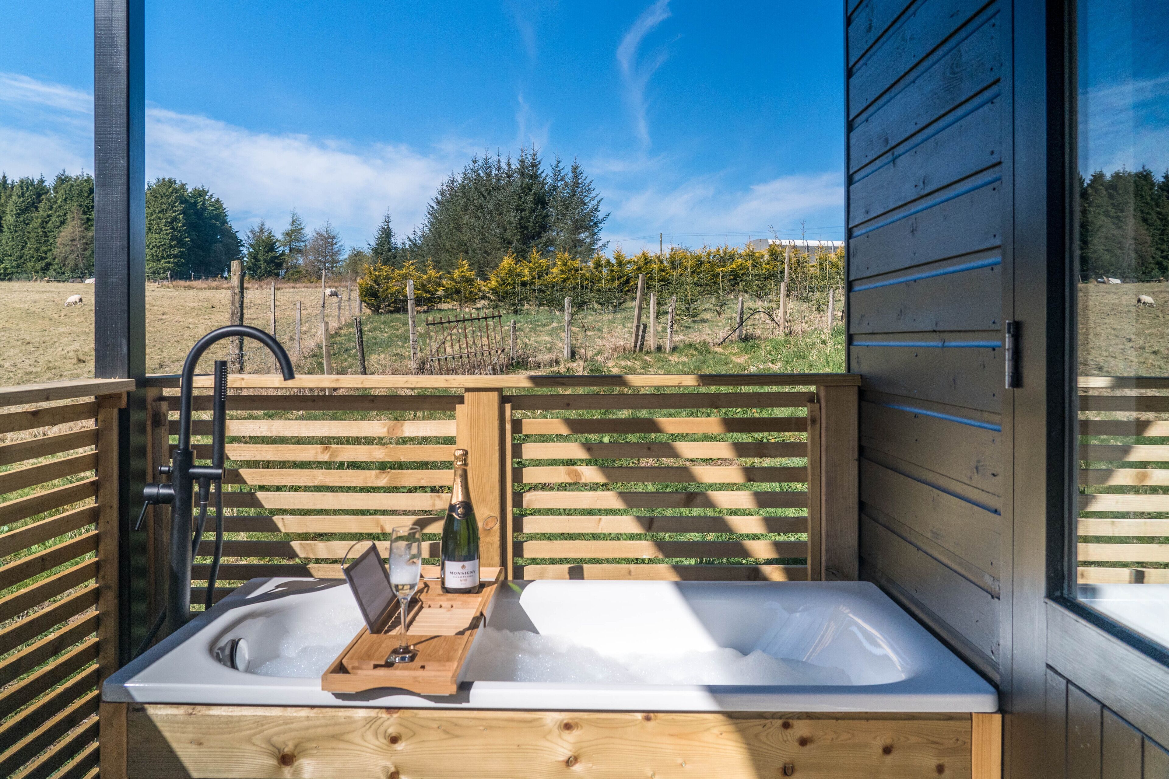 A wooden cabin with a built-in hot tub, a bottle of champagne, and a laptop on a wooden tray.
