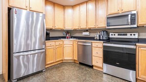 Una cocina moderna con armarios de madera y electrodomésticos de acero inoxidable, incluyendo un refrigerador, microondas, lavavajillas y horno.