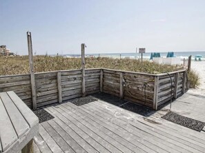 Une promenade en bois qui mène à une plage, avec une zone herbeuse et une vue dégagée sur l’océan.