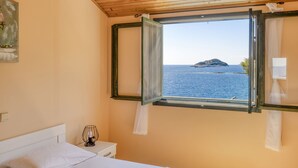 Ein Schlafzimmer mit Bett, Nachttisch mit Lampe und Fenster mit Blick auf das Meer und eine Insel.