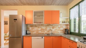 Eine Küche mit orangenen Schränken, einem Edelstahl-Kühlschrank, einem Geschirrspüler und einem Herd.