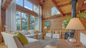 Un intérieur de chalet chaleureux avec un plafond en bois, de grandes fenêtres, une cheminée et un coin salon confortable.