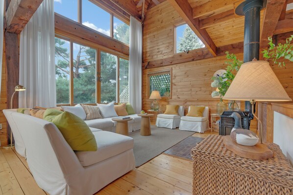 A cozy cabin interior with a wooden ceiling, large windows, a fireplace, and a comfortable seating area. - Waterfront, Fall 2026, Goose Rocks Beach, Kennebunkport (Kennebunkport)