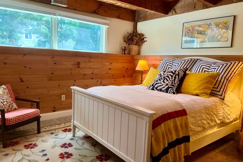 Ein Schlafzimmer mit einer holzverkleideten Wand, einem Bett mit weißem Gestell und einem Teppich mit Blumenmuster.