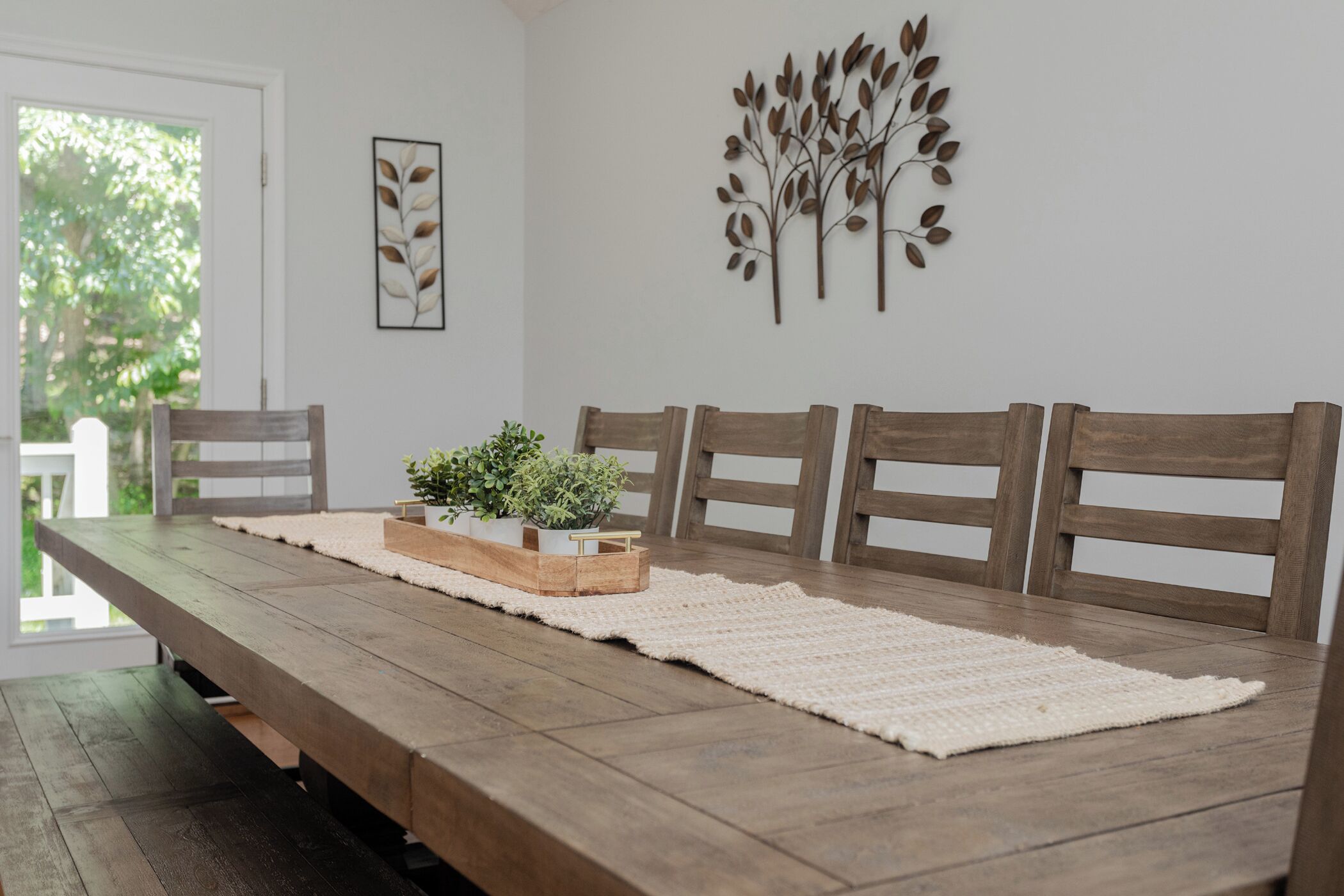 A dining area with a wooden table, four chairs, a white rug, and decorative wall art.