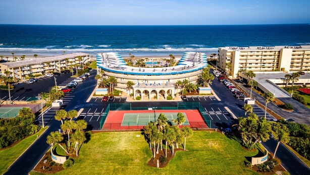 Hotel à beira-mar com edifício circular, estacionamento e quadra de tênis.