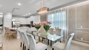 Une cuisine moderne avec des meubles blancs, une table à manger en verre et un lustre.