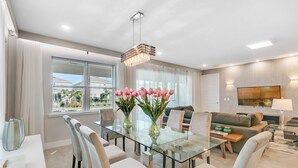 Un salon moderne avec une table à manger en verre, des sièges confortables, une grande fenêtre et un téléviseur à écran plat.