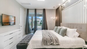 Une chambre moderne avec un grand lit, un téléviseur fixé au mur et une vue sur l’extérieur par la fenêtre.