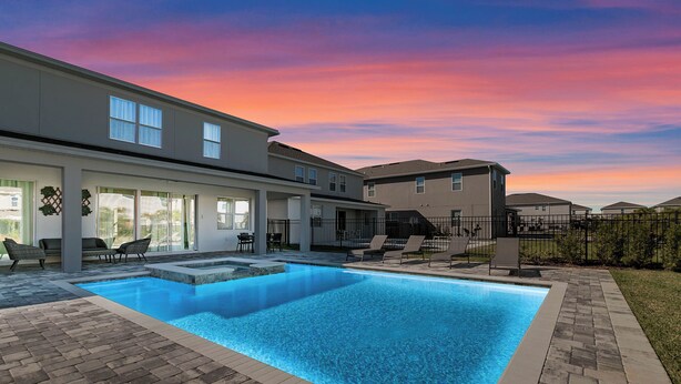 Un espace piscine résidentiel avec une maison moderne, des sièges d’extérieur et un ciel dégagé.