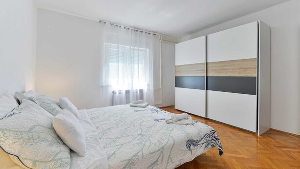 A bedroom with a bed, a wardrobe, and a window with sheer curtains. - Holiday Home Vesna with pool and children area (Suhovare)