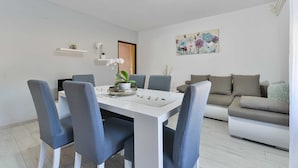 A modern living room with a white sofa, a dining table with chairs, and a painting on the wall. - Holiday Home Vesna with pool and children area (Suhovare)