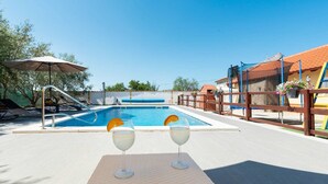 A poolside area with a clear blue pool, two glasses of a beverage with orange slices, and a wooden fence. - Holiday Home Vesna with pool and children area (Suhovare)