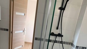 A shower area with a glass door, a black tiled floor, and a white tiled wall with a decorative border. - Rent a villa overlooking the Gulf of Valinco (Sartène)