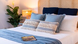 Ein ordentlich bezogenes Bett mit einer blauen Decke, zwei Makramee-Kissen und einer Zeitschrift darauf.