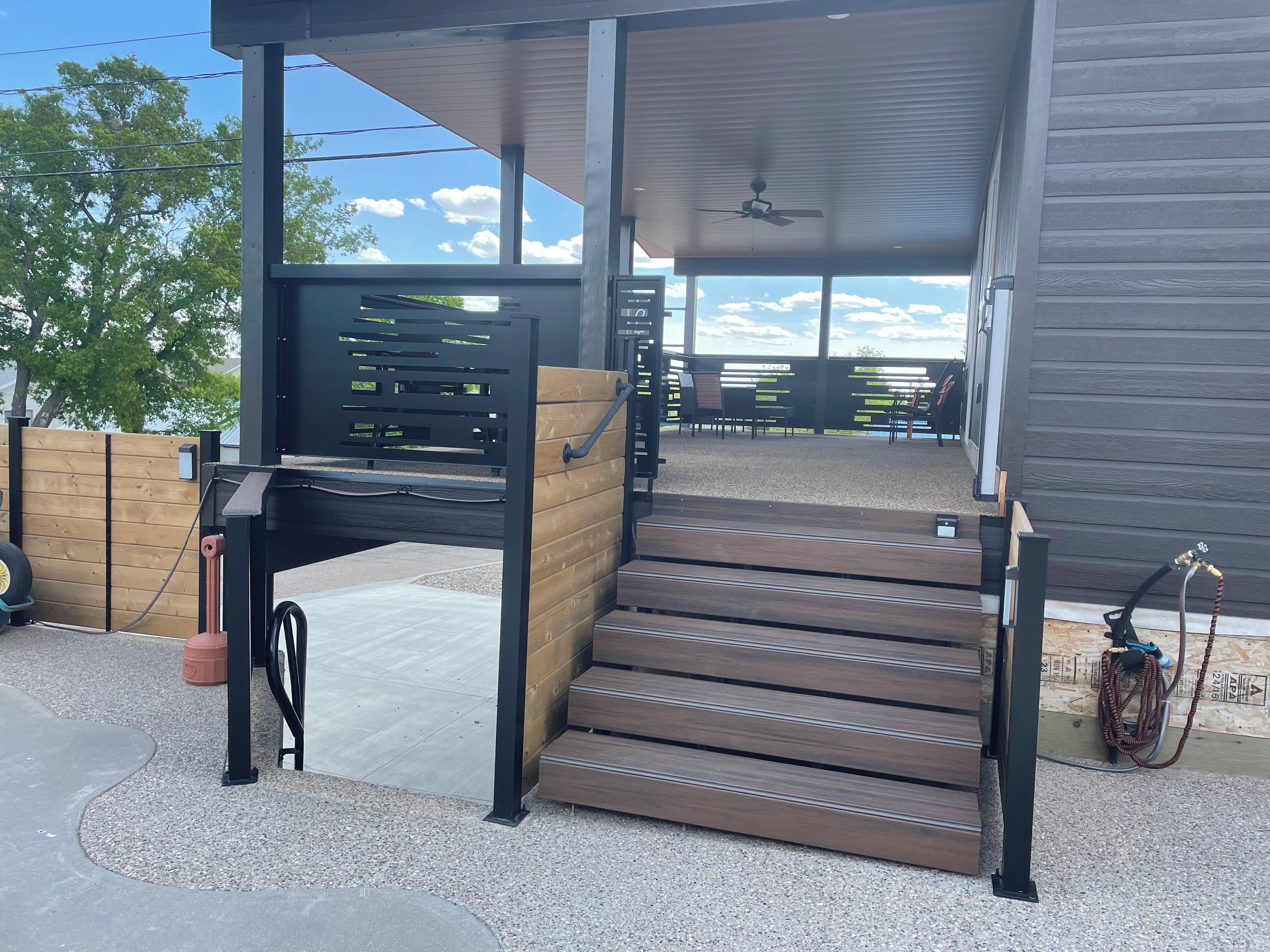 A covered outdoor seating area with a wooden bench, a staircase, and a hose connected to a building.