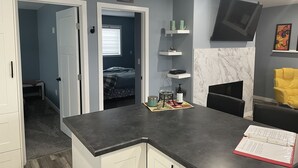 A modern kitchen with a dark countertop, white cabinets, and a small island. There is a bed visible through an open door in the background. -  Loft 902 with Sunsets from the 14x32 covered deck almost every morning! (Estevan)