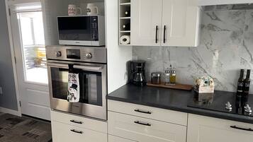 Eine Küche mit integriertem Mikrowellenherd, Backofen und Kaffeemaschine. Es gibt Schränke mit Griffen, eine Arbeitsplatte mit Kaffeemaschine und eine dekorative Schachtel mit Blumen.
