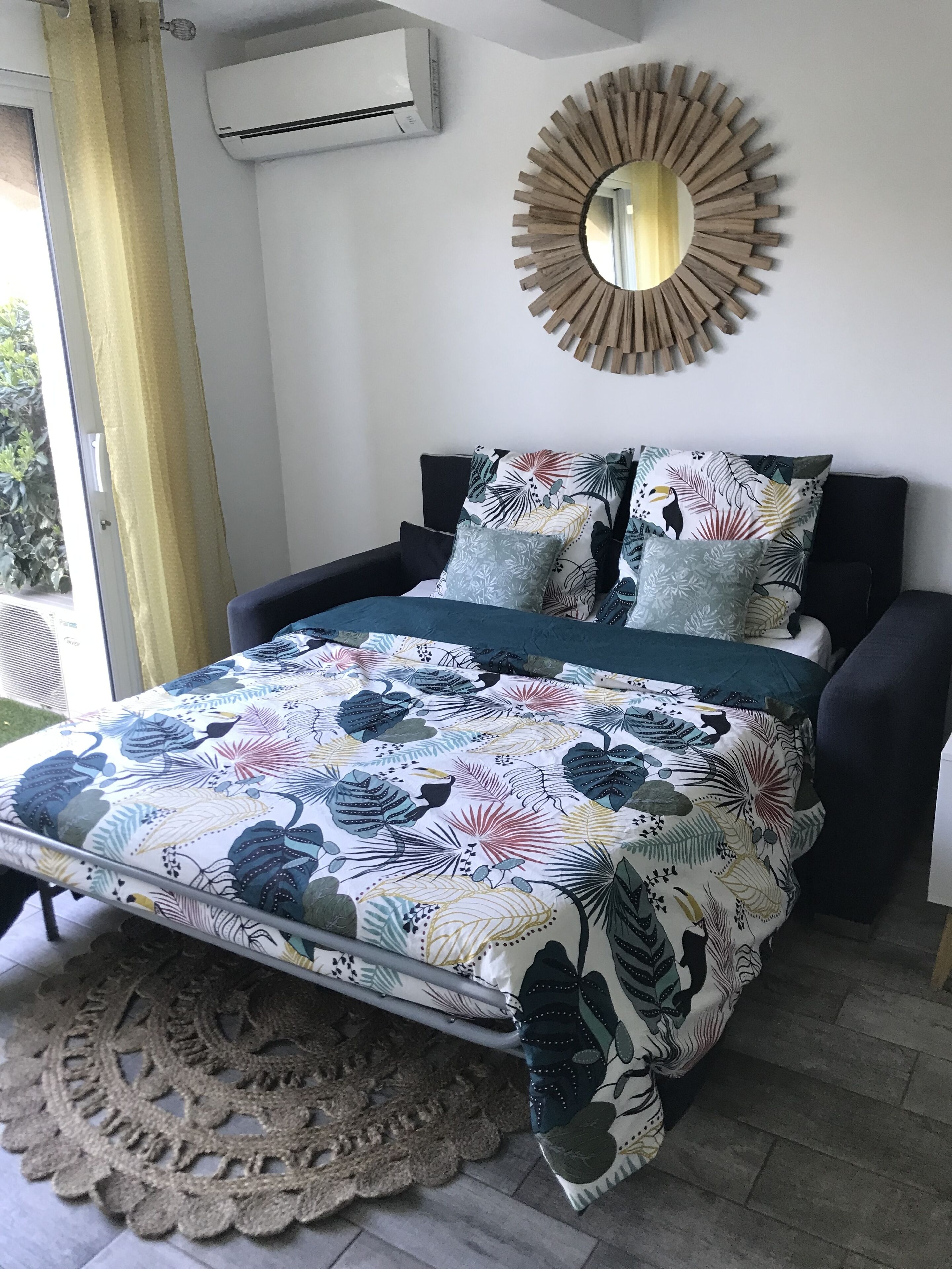 Une chambre à coucher avec un lit, un miroir rond et une fenêtre avec des rideaux.