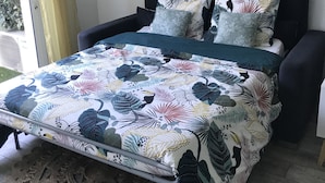 A bedroom with a bed, a round mirror, and a window with curtains. - Studio 100m from the beach, patio, car park, air conditioning (Six-Fours-les-Plages)