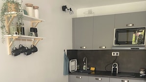 A modern kitchen with grey cabinets, a microwave, and a sink. There is a dining table set with plates, glasses, and cutlery. - Studio 100m from the beach, patio, car park, air conditioning (Six-Fours-les-Plages)
