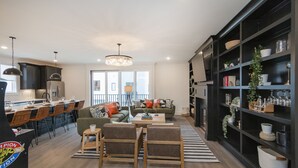 Une cuisine moderne avec des meubles de couleur sombre, un coin repas avec des chaises en bois et un salon avec un canapé et une table basse.