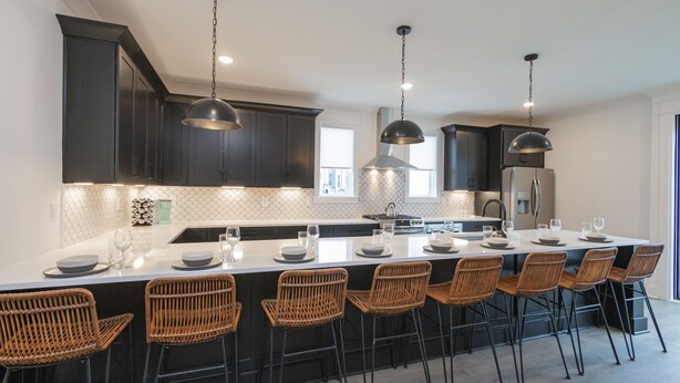 Une cuisine moderne avec des meubles de couleur sombre, un grand îlot central doté de tabourets, un éclairage suspendu et une vue sur l’extérieur.