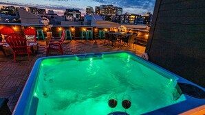 Un espace piscine sur le toit, comprenant un jacuzzi, des sièges et une vue sur la ville au crépuscule.