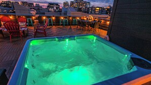 Un jacuzzi con iluminación verde, rodeado de asientos exteriores y vistas a la ciudad.