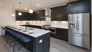 Una cocina moderna con armarios oscuros, electrodomésticos de acero inoxidable y una isla central con taburetes de bar.