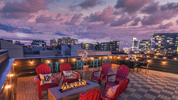 Una terraza en la azotea con sillas Adirondack rojas, una fogata y luces colgantes.